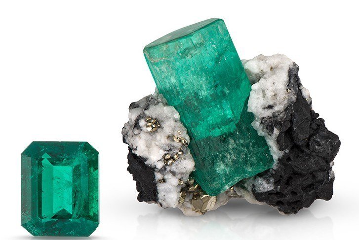 Emerald-cut green emerald next to an emerald crystal on black and white matrix
