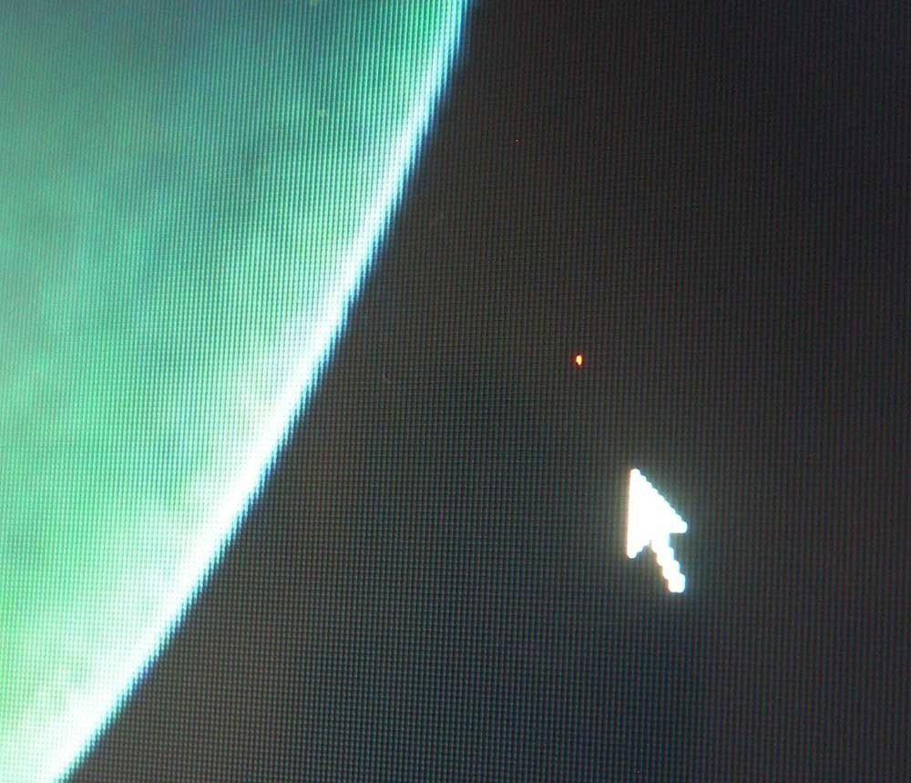 Close-up of a screen showing a single tiny red pixel defect on a dark background beside the mouse pointer