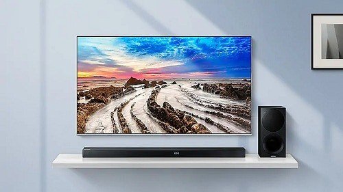 Wall-mounted Samsung TV above a soundbar and a separate speaker on a shelf