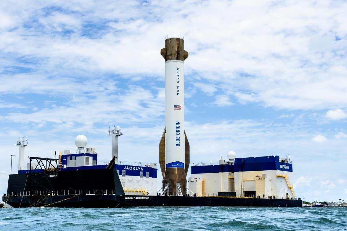 A Blue Origin booster standing upright on a landing vessel at sea under a cloudy sky