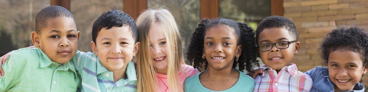 Six smiling young children posed together outdoors