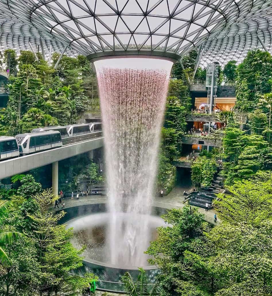 The Rain Vortex waterfall inside Jewel Changi Airport with a Skytrain crossing above it