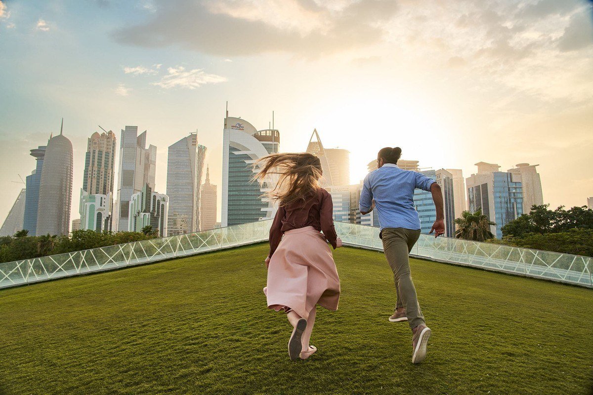 Couple running across a rooftop lawn with the Doha skyline behind them