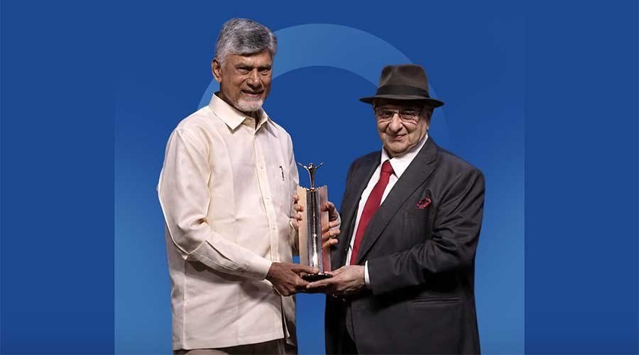 Two men on a blue stage backdrop at the Economic Times Awards for Corporate Excellence, one holding a trophy, as Cyrus Poonawalla receives a lifetime achievement award