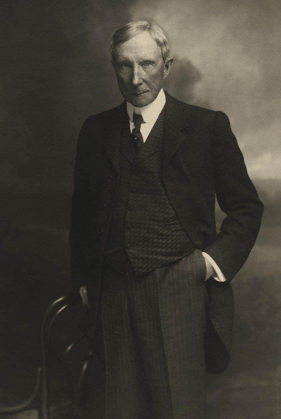 Studio photograph of John D. Rockefeller standing in a dark suit with one hand in his pocket