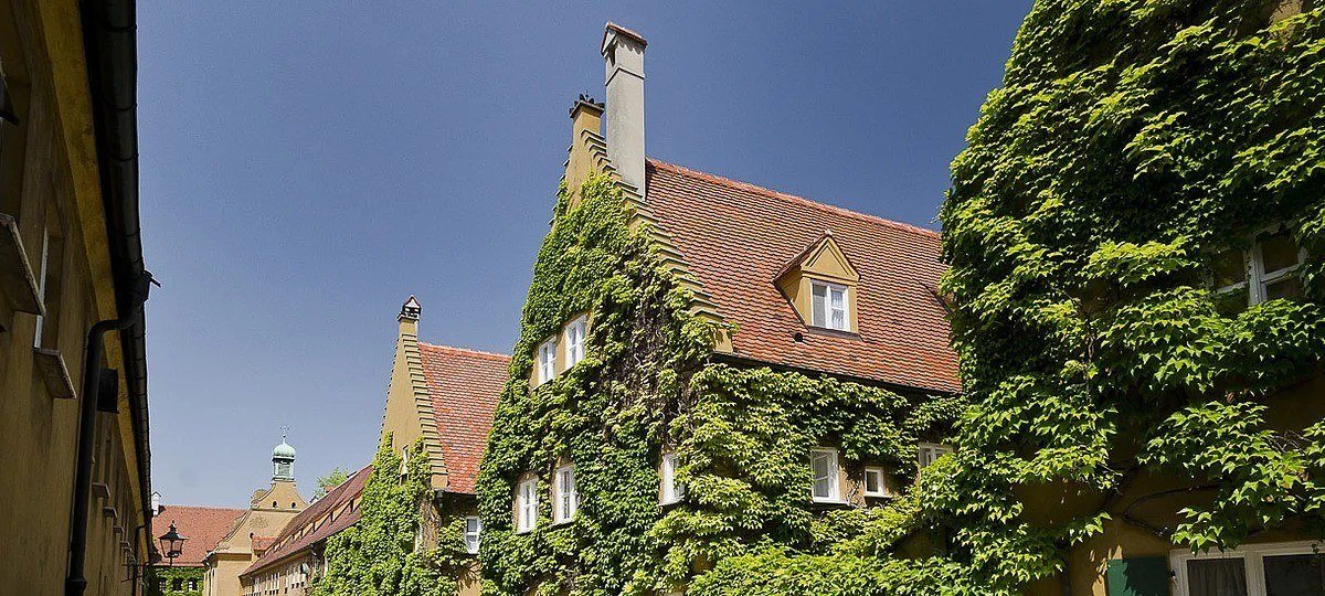 Ivy-covered red-roofed houses of the Fuggerei in Augsburg under a blue sky