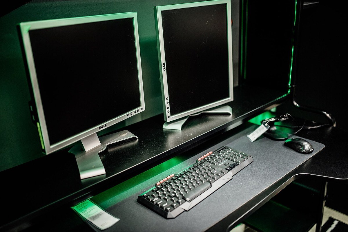 Two Dell monitors side by side on a dark desk with a keyboard and mouse lit in green