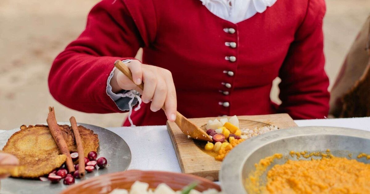 Costumed interpreter in a 17th-century doublet serving corn cakes, cranberries, root vegetables and pumpkin at Plimoth Patuxet